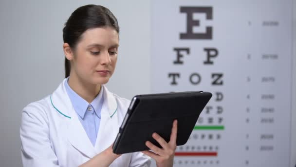 Lady optometrist sprawdzanie wyników w tablecie i uśmiechnięty do aparatu, technologii — Wideo stockowe