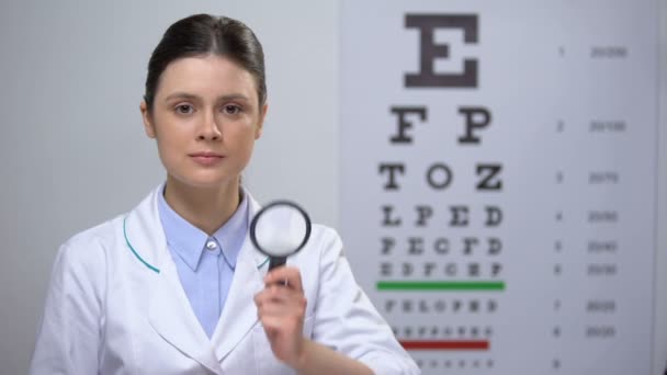 Optometrista sonriente mirando a través de lupa y sonriendo, prueba de vista — Vídeos de Stock