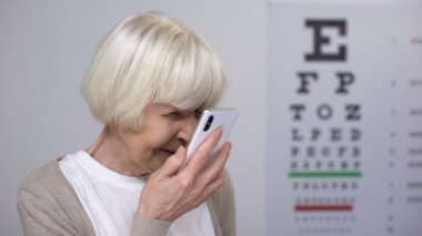 Bayan emekli gözlük koyarak, gülümseyerek ve akıllı telefon, körlük okuma
