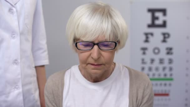 Optician comforting aged lady trying to read book, patient suffering poor vision — Stock Video