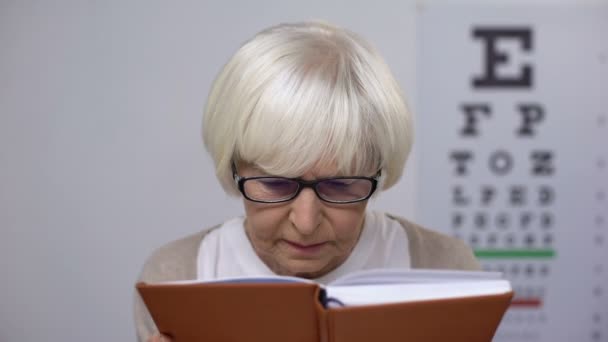 Mujer jubilada en el libro de lectura de gafas, infeliz con la mala visión, problema — Vídeos de Stock