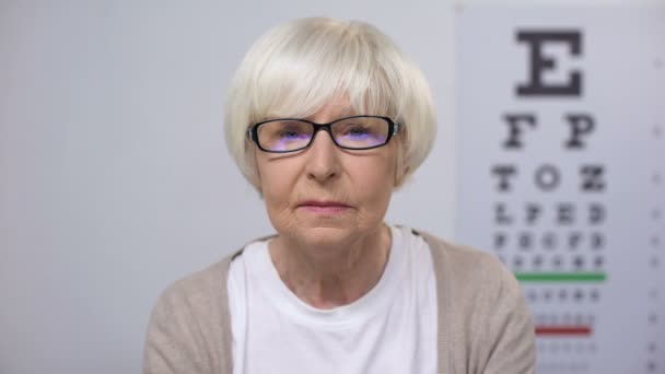 Mujer mayor en anteojos leyendo periódico y sacudiendo la cabeza, riesgo de cataratas — Vídeos de Stock