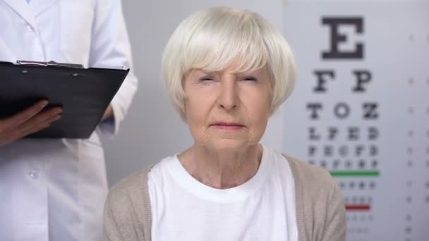 Ηλικίας κυρία επίσκεψη oculist, γιατρός γράφοντας συστάσεις, ηλικιωμένοι φροντίδα θέα — Αρχείο Βίντεο