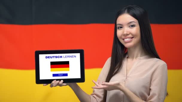 Señora celebración de la tableta con aprender alemán aplicación, bandera de Alemania en el fondo, la educación — Vídeos de Stock