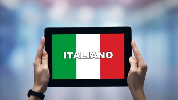 Las manos femeninas sosteniendo la tableta con palabra italiana contra la bandera nacional, aplicación en línea — Vídeos de Stock