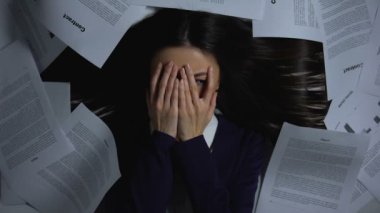 Korkmuş kadın yüzünü kapatıyor, evrak yığınına bakıyor, işe başlamaktan korkuyor