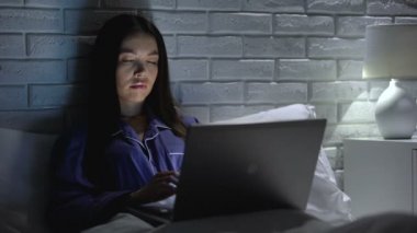 Geceleri yatakta dizüstü bilgisayar üzerinde çalışan uykulu kadın, sıkıcı proje de motivasyonsuz