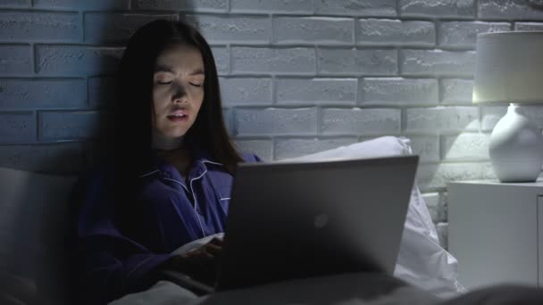 Молодая женщина страдает головной болью, работает в спальне поздно ночью, трудоголик — стоковое видео