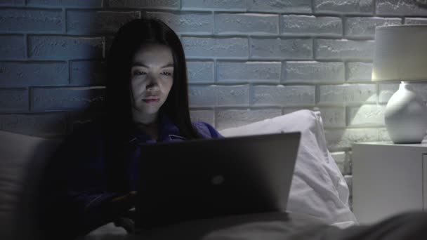 Uykulu asyalı kadın gece toplantı süresi, mesai başında yatakta dizüstü bilgisayar üzerinde çalışan — Stok video