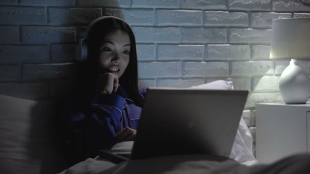 Усміхнена жінка в навушниках дивиться відео вночі, залежність від соціальних мереж — стокове відео