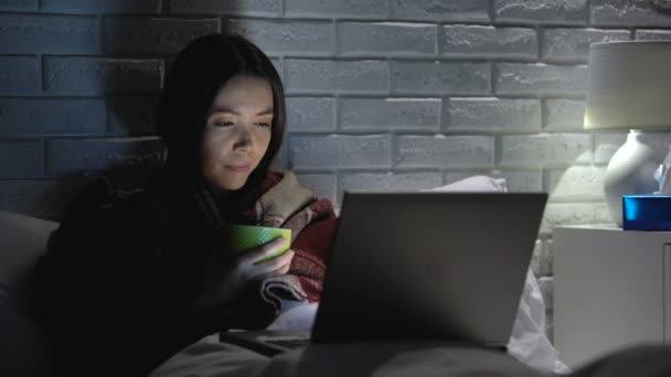 Girl feels sick lying in bed, drinking tea, watching movie on laptop, flu season — Stock Video