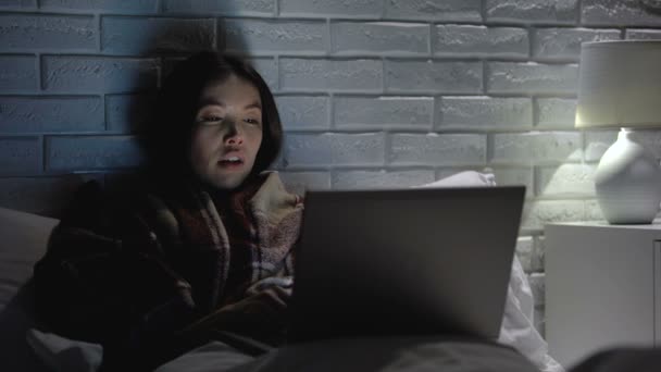 Girl sneezing hard, lying in bed watching movie on laptop at night, flu symptoms — Stock Video