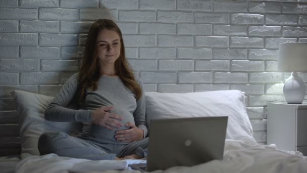 Heureuse femme enceinte caressant le ventre, regarder des vidéos éducatives sur Internet — Video