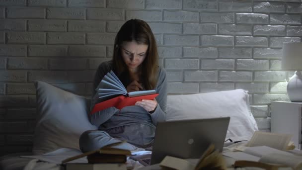 Estudiante cansada leyendo libros y portátil, preparándose para el examen tarde en el dormitorio — Vídeos de Stock