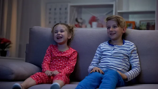 Happy children watching comedy film sitting sofa, having fun, laughing together