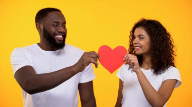Mutlu genç çift kırmızı kağıt kalp tutan ve gülümseyen, gerçek aşk ve bakım