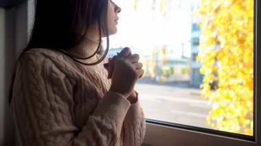 Pencere nin üzerinde oturan kadın, pencereden bakıyor, arkadaşını bekliyor.