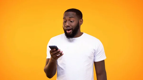 黄色の背景にスマートフォンのアプリケーションを使用して驚いた黒人男性 — ストック写真