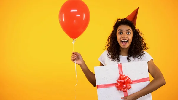 プレゼントと赤い風船を保持するパーティー帽子で興奮した若い女性 休日のイベント — ストック写真