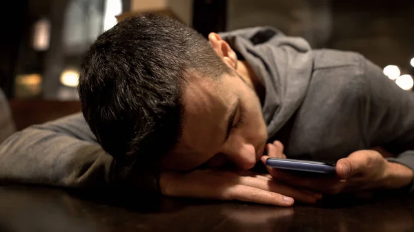 Tired man sleeping on table in restaurant, holding smartphone, busy lifestyle