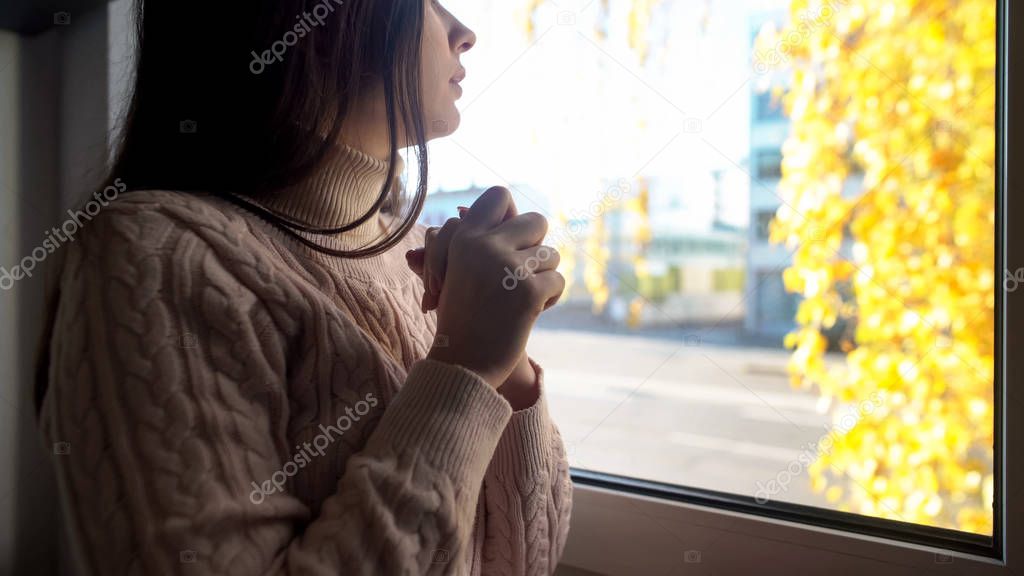 Woman sitting on window sill, looking through window, waiting for friend