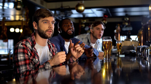 Nervous multiethnic men watching match in bar, hoping for team scoring goal