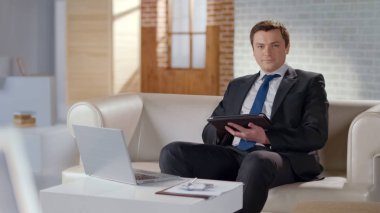 Ofiste tablet kullanarak takım elbiseli genç adam, iş yönetmek için modern teknolojiler