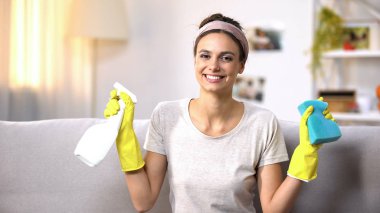 Kamera, ev işi temizlik sprey ve sünger gösteren eldiven gülümseyen kadın