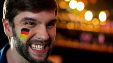 Alman spor takımının mutlu taraftarı yanağında bayrakla maç izlerken gülümseyen