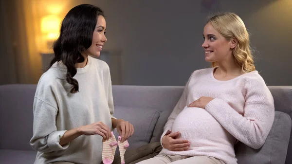 年轻女子呈现粉红色小袜子给她怀孕的朋友 婴儿淋浴 — 图库照片
