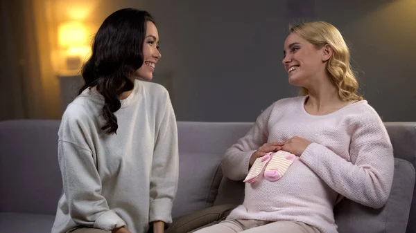 微笑的孕妇拿着小袜子在她的肚子 婴儿淋浴与朋友 — 图库照片