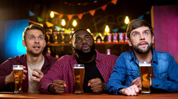 Three male friends watching breaking news on big screen in bar, evening leisure