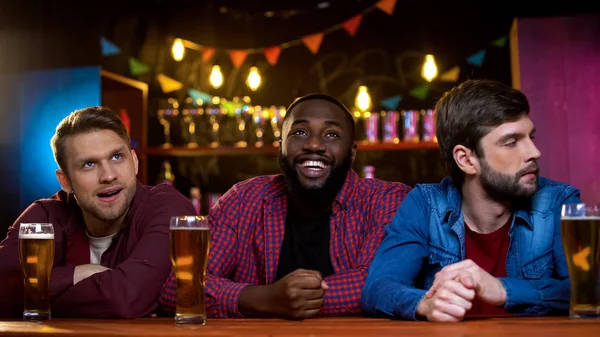 バーでテレビを見て微笑むアフリカ系アメリカ人の男性 白人の友人は動揺 — ストック写真