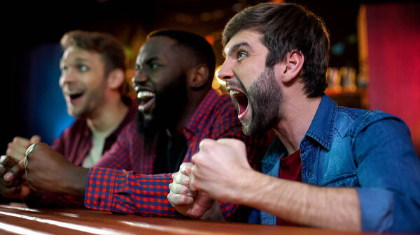 Extremely happy multiracial friends celebrating victory of national boxer in bar