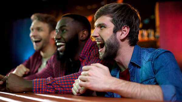 Cheerful multiracial friends screaming, celebrating sports team victory in bar