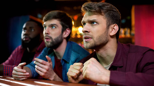 Caucasian and black male friends watching football game in bar, team losing