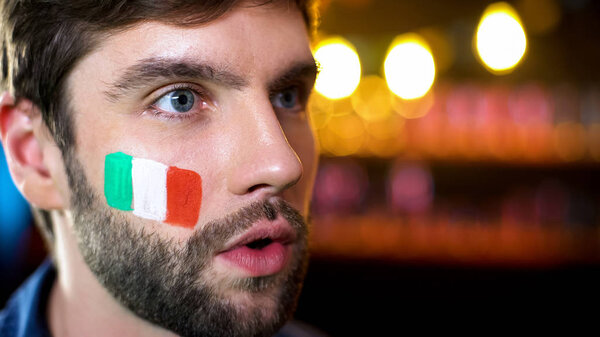 Нервный человек с итальянским флагом на щеке смотрит новости, результаты выборов на телевидении
