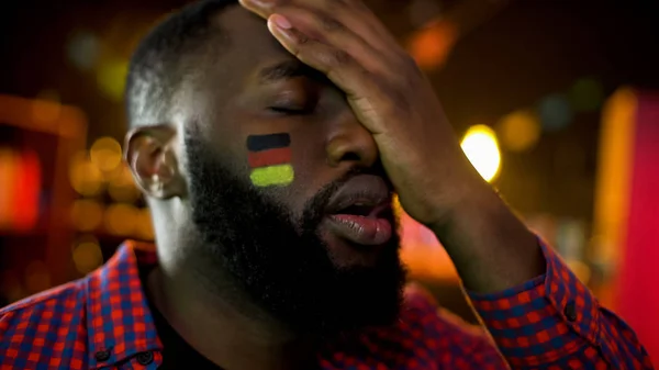 フェイスパームを作る頬に旗を持つ失望したドイツのサッカーファン チームの敗北 — ストック写真