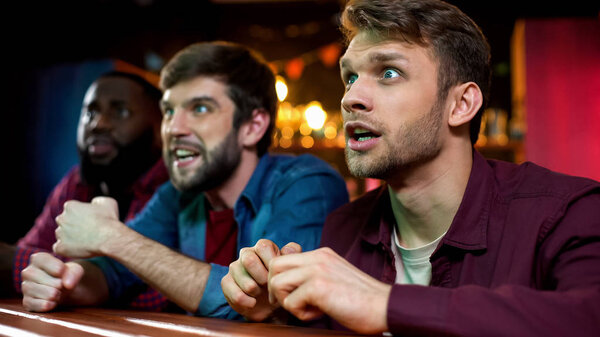 Multiracial fans celebrating favorite team scoring goal, watching game in pub