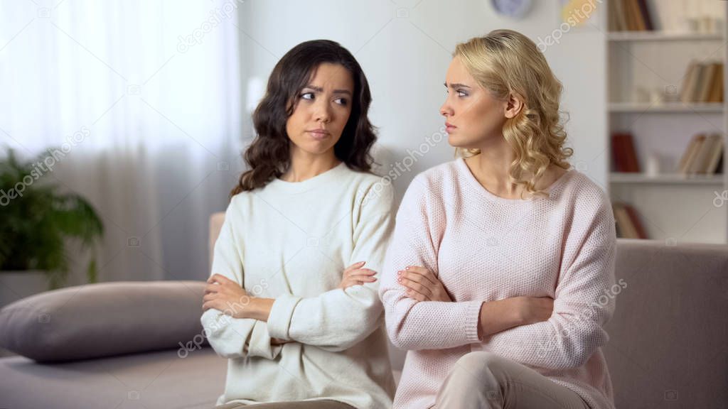 Two female friends reconciling after quarrel, sitting on sofa with friends