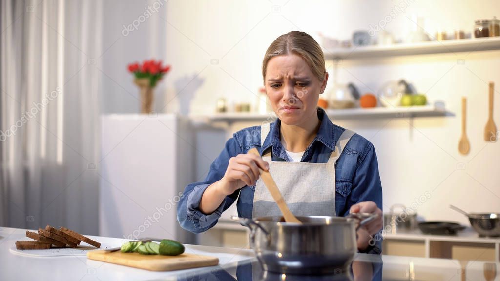 Girl disgusted with stinky meal on stove, spoiled ingredients, untasty food