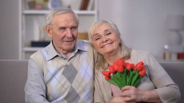 Älteres Paar umarmt sich zu Hause, Frau hält Tulpenstrauß, Jubiläumsgeschenk — Stockvideo