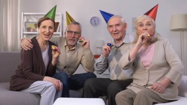 Cheerful aged people in birthday hats blowing in party horn, celebration, party — Stock Video