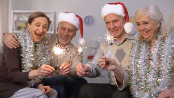 Men in Santa Claus hats and women wrapped in tinsels holding sparklers, New Year — Stock Video