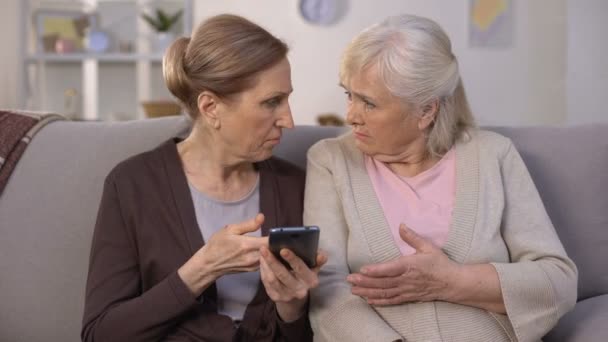 Две зрелые дамы пытаются справиться со смартфоном, проблемы с технологиями — стоковое видео