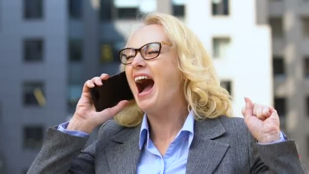 Mature female office worker rejoicing good news from phone about raising salary — Stock Video