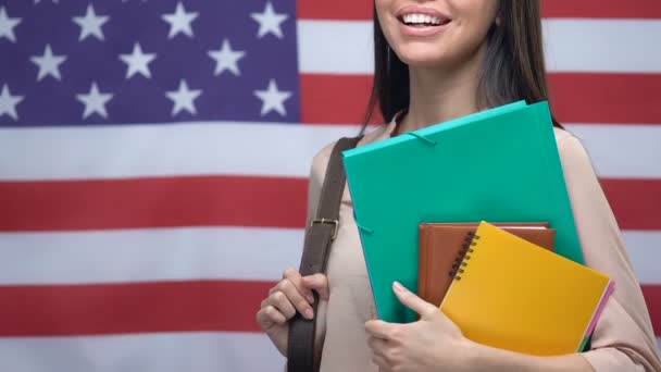 Улыбающаяся женщина с блокнотами на фоне американского флага, степень бакалавра — стоковое видео