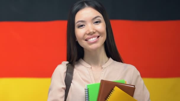 Улыбающаяся женщина с блокнотами на фоне немецкого флага, на курсе академии, студентка — стоковое видео