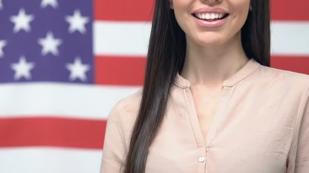 Улыбающаяся женщина показывает паспорт против американского флага, получает гражданство США — стоковое видео