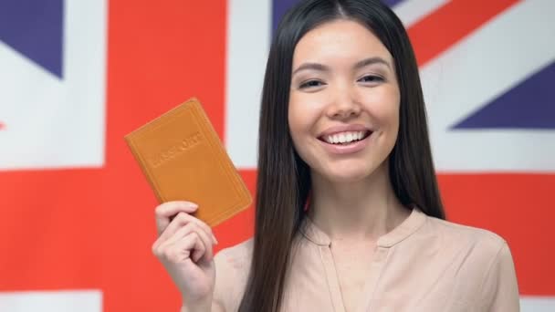 Gelukkige vrouw toont paspoort, vlag van Groot-Brittannië op de achtergrond, reisbureau — Stockvideo